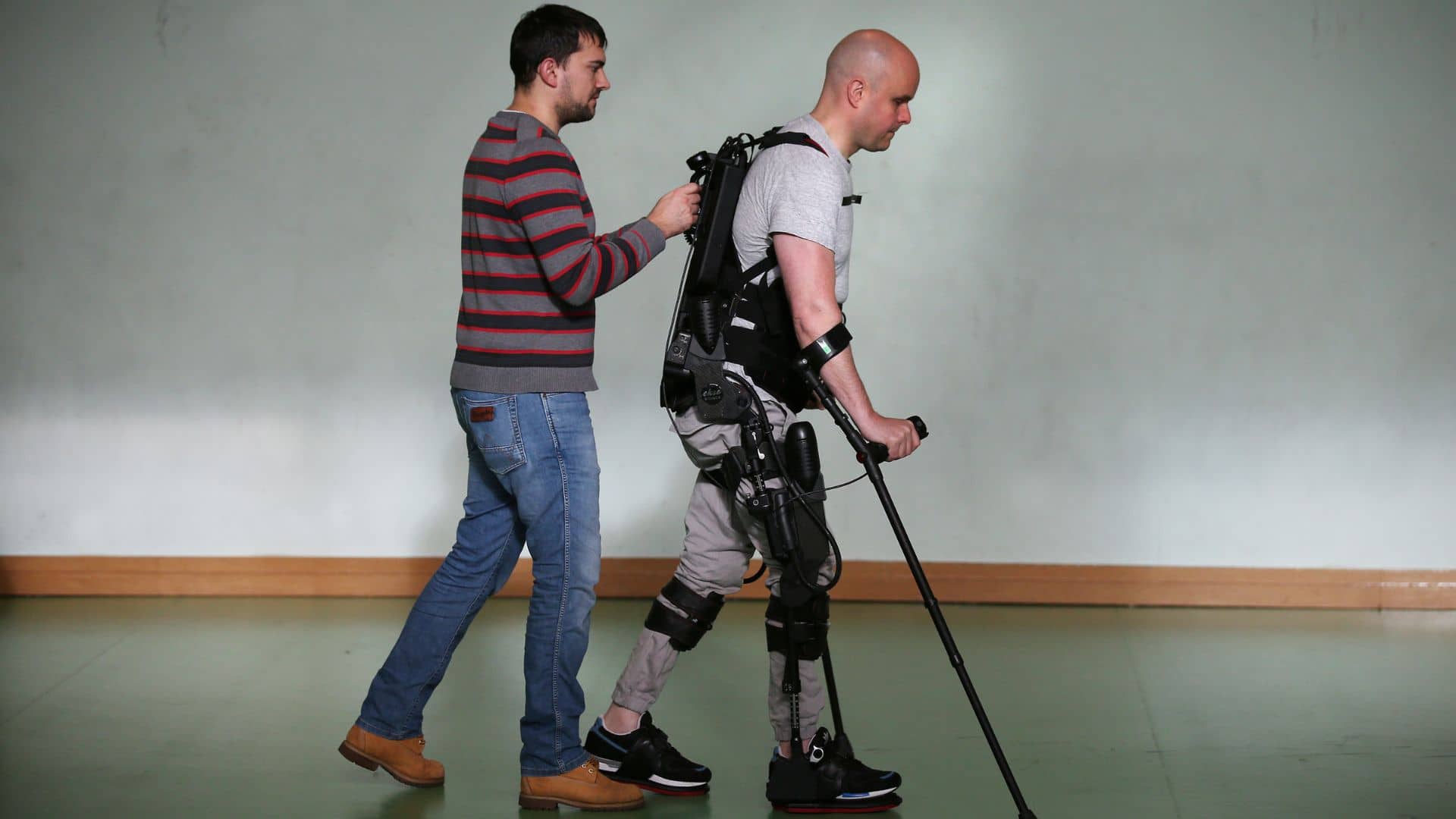 Mark Pollock walking in Ekso suit with carer. 